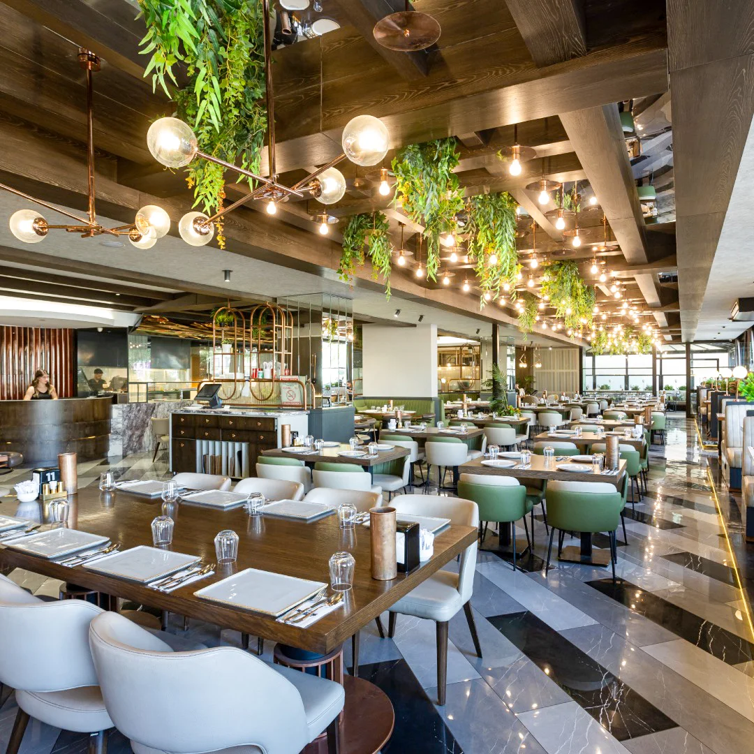 Restoranın derinlikli görünümü, tavandan sarkan bitki aranjmanları, çoklu sarkıt aydınlatmalar ve ayna detaylı kolonlar, NDO Mimarlık Diyarbakır