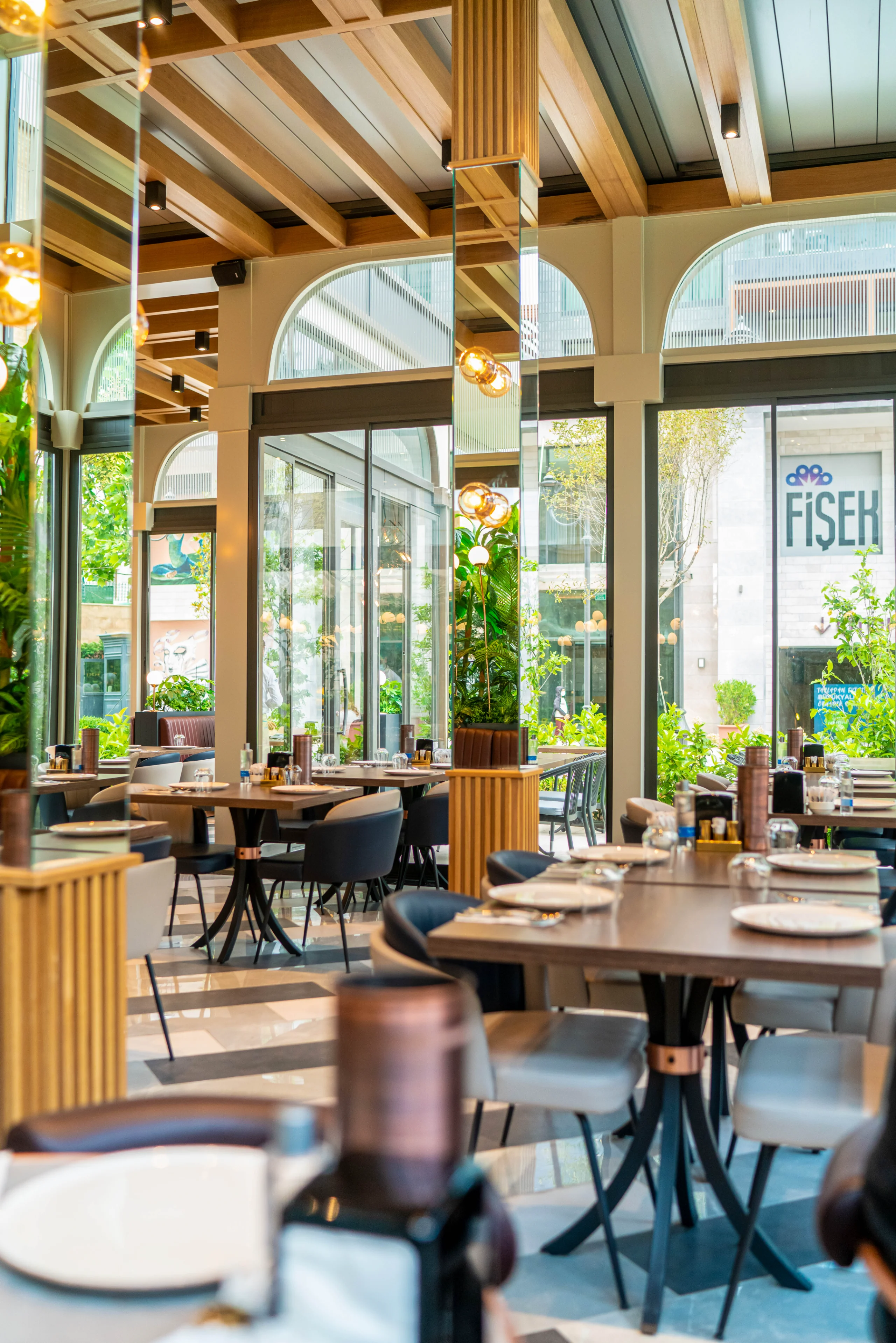 Geniş yapraklı salon bitkileri ve bakır yaprak formlu özel tasarım zemin aydınlatmaları, restoran atmosferi, NDO Mimarlık