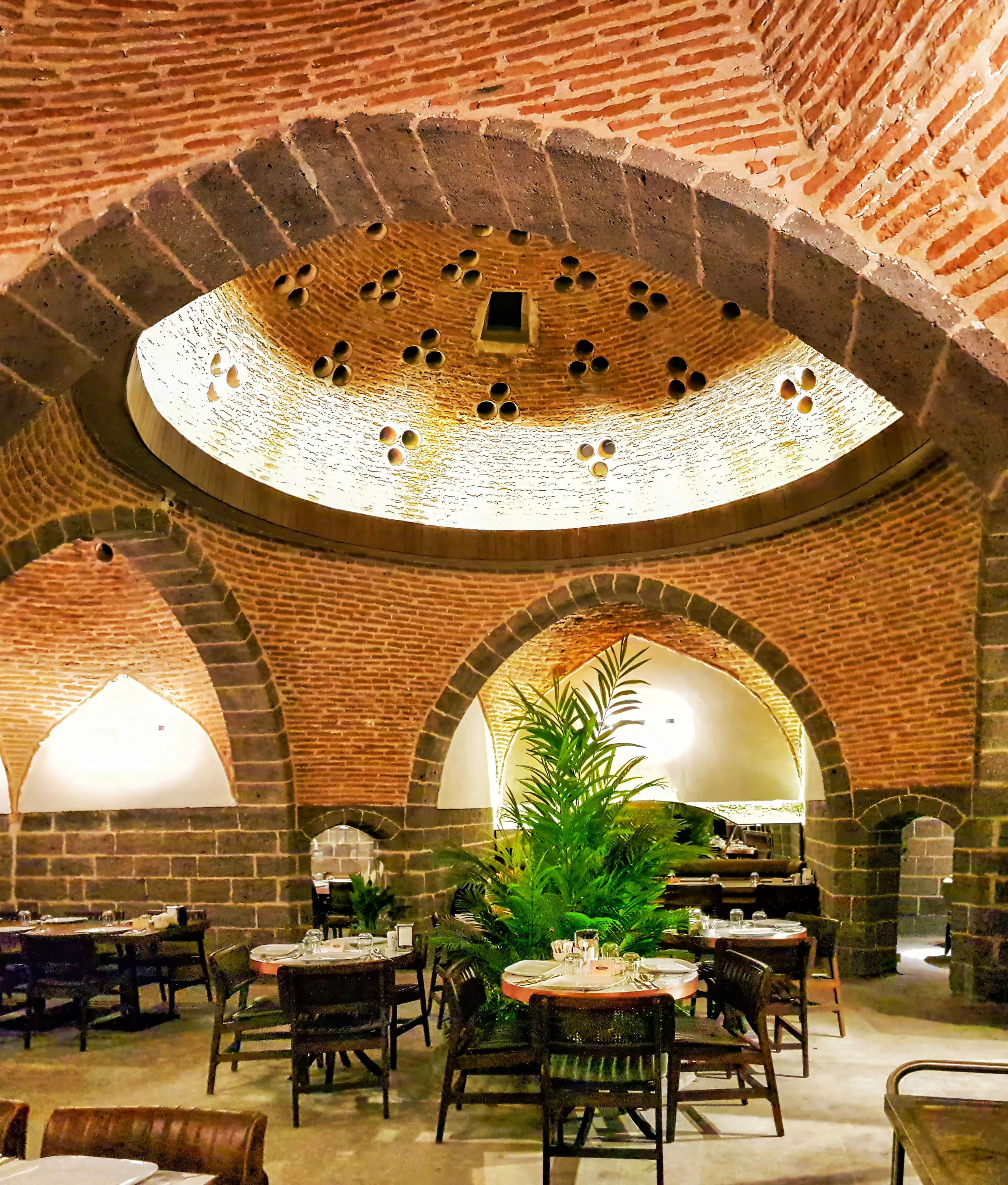 Fırın-ci Sur ana salonunda kubbeli tavan, merkezi bitkisel ada ve çağdaş restoran oturma düzeni.