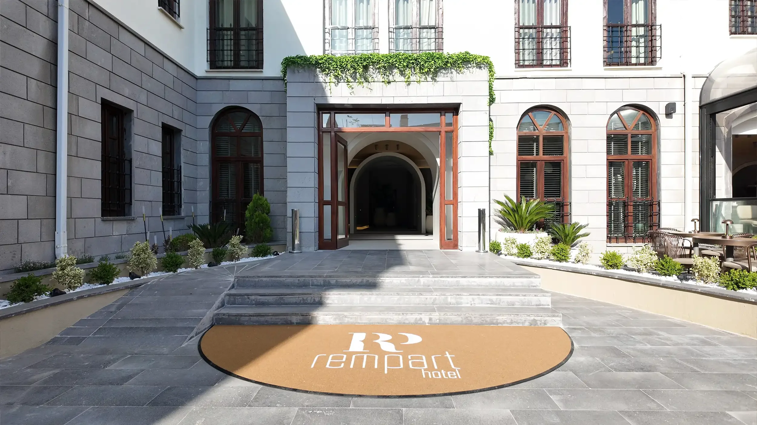 Rempart Hotel gece avlusunda sıcak peyzaj aydınlatmaları, açık oturma masaları, cam örtülü restoran bölümü ve tarihi taş cephelerle kurgulanan butik otel atmosferi, NDO Mimarlık