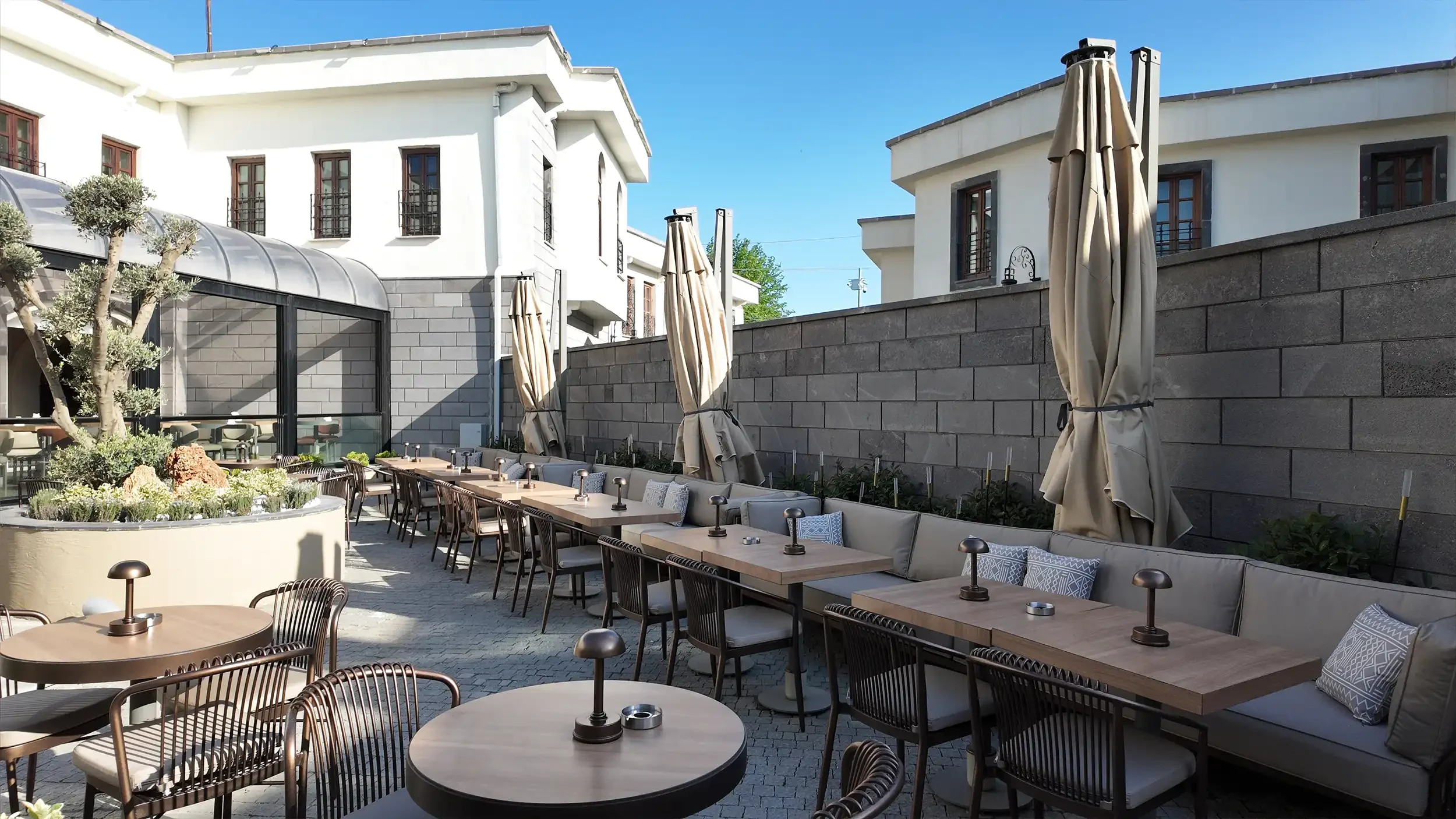 Rempart Hotel suit odasında dokulu taş başlık duvarı, yumuşak yatak tekstili, ahşap yüzeyler, sarkıt aydınlatmalar ve oturma köşesiyle tasarlanan konforlu otel odası, NDO Mimarlık