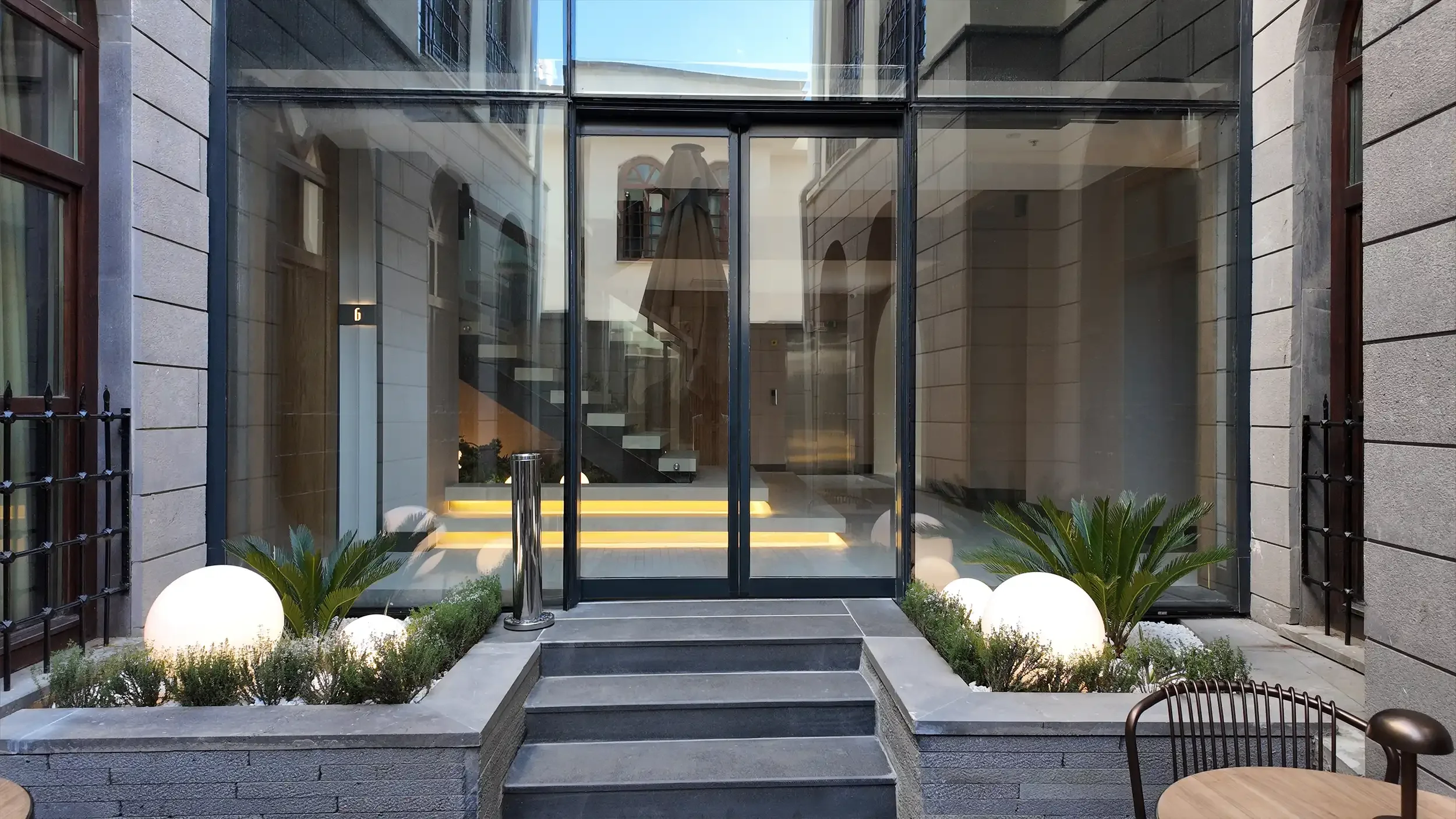 Rempart Hotel cam örtülü restoran alanında doğal ışık alan yemek düzeni, yuvarlak ve kare masalar, modern sandalyeler ve taş avlu ilişkisiyle tasarlanan yemek mekânı, NDO Mimarlık