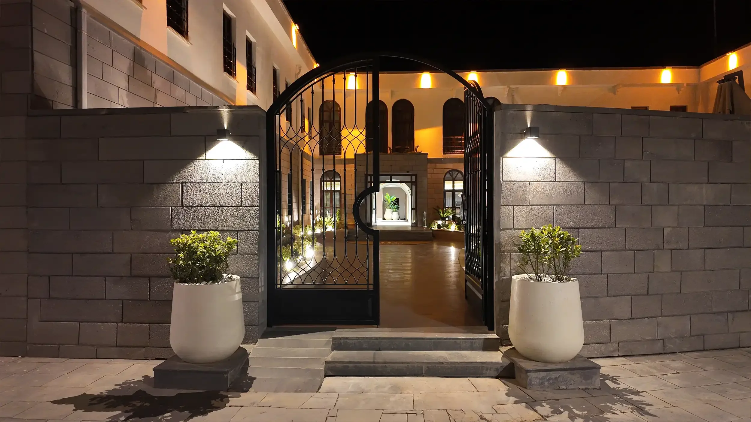 Rempart Hotel avlusunda gri taş zemin, kavisli peyzaj sınırları, açık oturma grupları ve otel logosunu taşıyan giriş yönlendirmesiyle tasarlanan dış mekân karşılama alanı, NDO Mimarlık