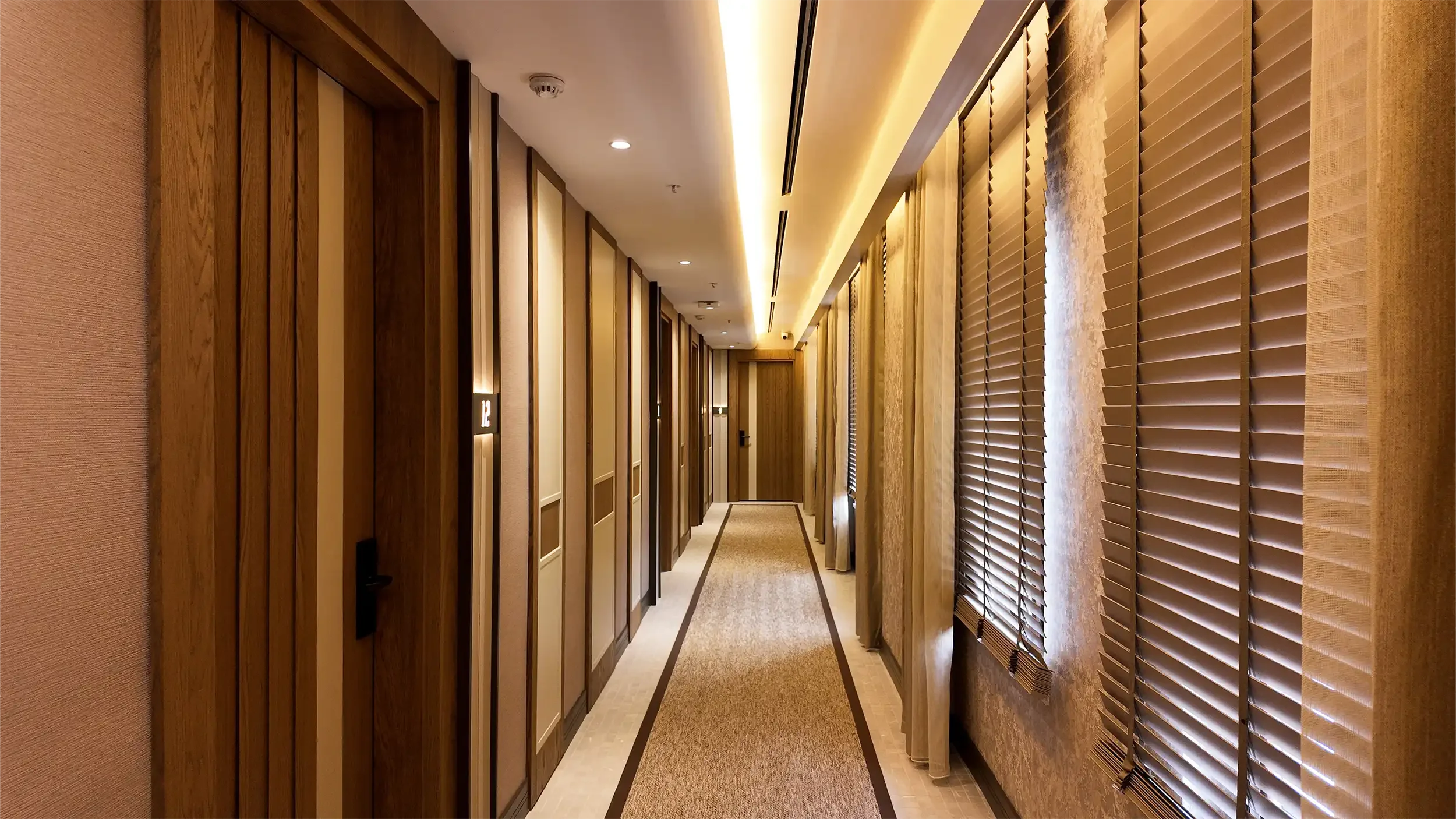 Rempart Hotel suit odasında doğal ışık alan pencere önü oturma köşesi, yuvarlak sehpa, tekstil perdeler ve sakin renk paletiyle tasarlanan dinlenme alanı, NDO Mimarlık