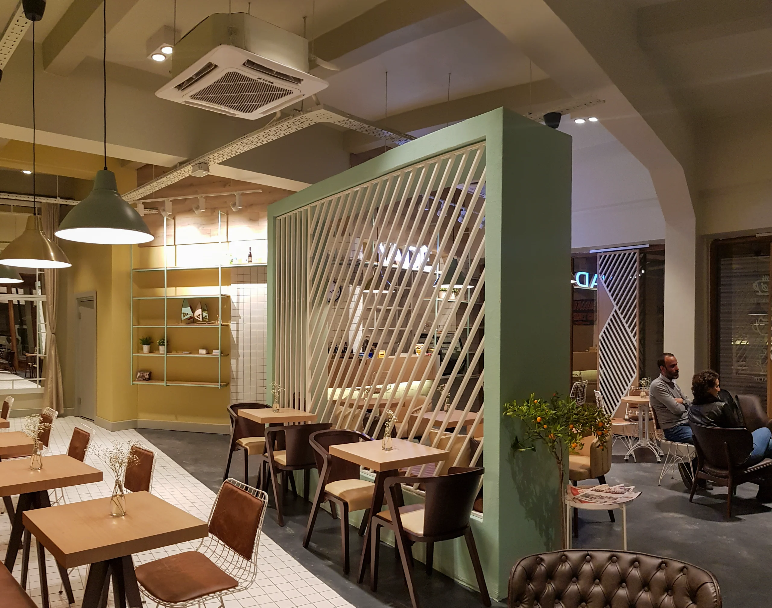 Pastel yeşil çerçeveli diyagonal seperatör, farklı oturma grupları, ahşap masalar ve endüstriyel tavan kurgusuyla tasarlanan Yade Kafe, NDO Mimarlık